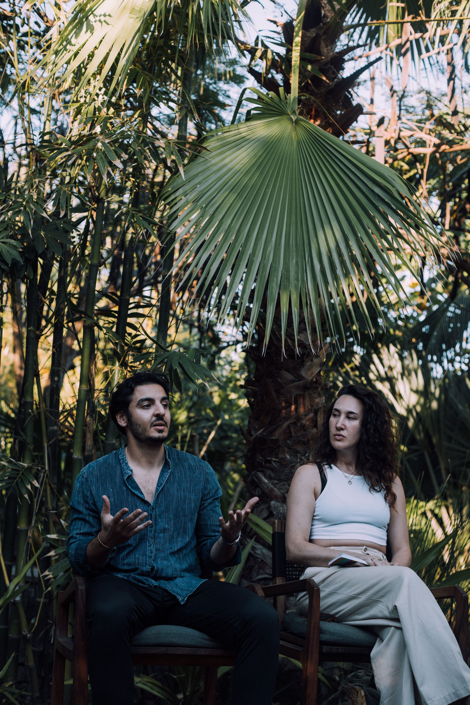 Faris Batayneh in a working conversation, seated outdoors under palm fronds